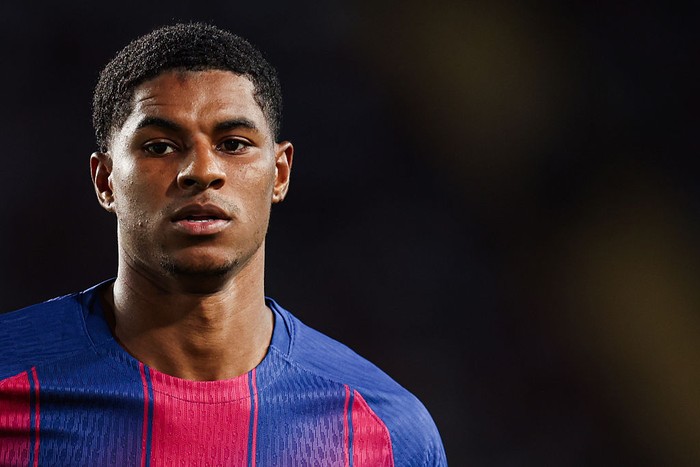 Close-up portrait of a male footballer in a blue jersey with pink accents, looking forward with a focused expression.