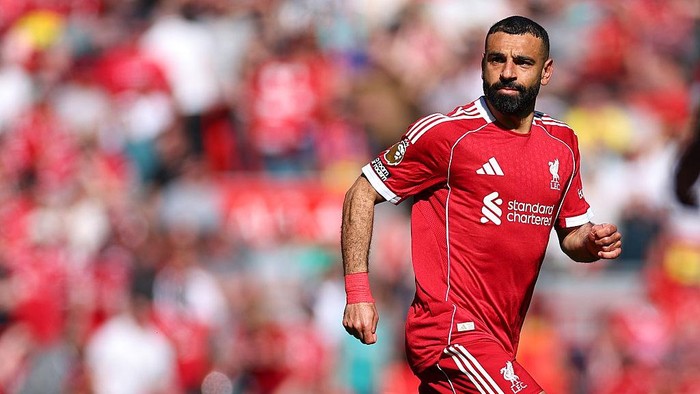Soccer player in a red Liverpool jersey runs on the field during a match with a blurred crowd behind him.