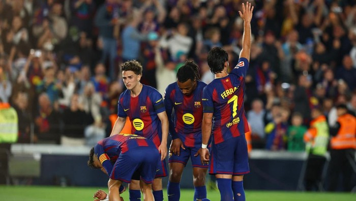 Barcelona players in blue-red kit on the pitch, crowd in background, one player raises his hand.”] ,
