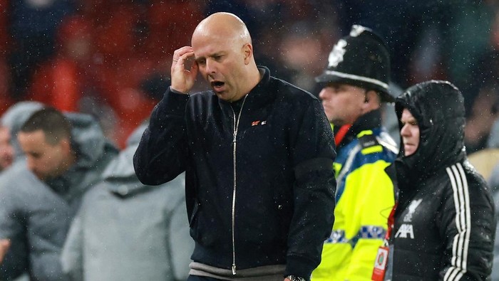 Soccer coach with hand to ear on a rain-soaked sideline, focused during the match.