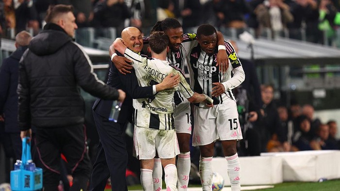 Juventus players and a coach huddle together in a group hug on the sideline after a match, wearing black-and-white striped kits.