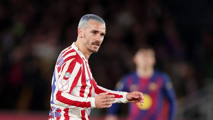 Footballer in a red-and-white striped kit gestures during a match, with a blurred opponent in the background.