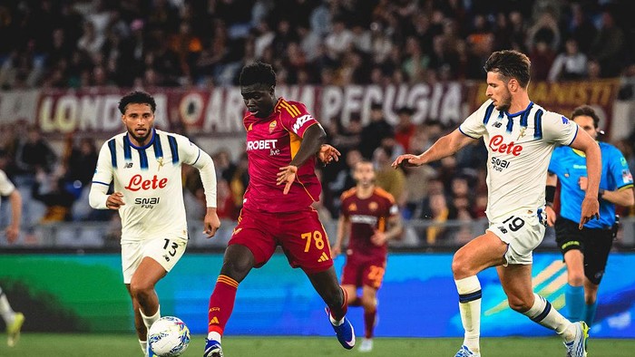 Roma player in maroon kit (#78) dribbles as two Napoli players in white-blue defend near the ball with a crowded stadium behind them