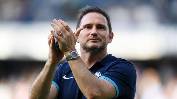 Soccer coach in a navy polo shirt clapping on the field during a match