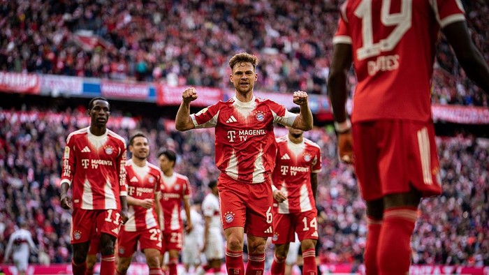 Soccer players in red and white uniforms celebrate on a packed stadium; central player raises fists in triumph.