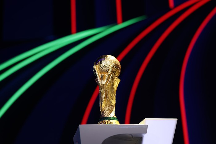 FIFA World Cup trophy on a podium with neon green and red light arcs in a dark background