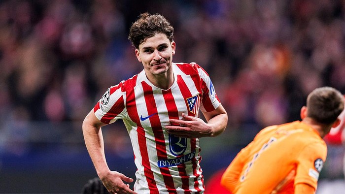 Atlético Madrid player in red-and-white stripes runs with the ball during a match, with an opposing orange-jersey player nearby.