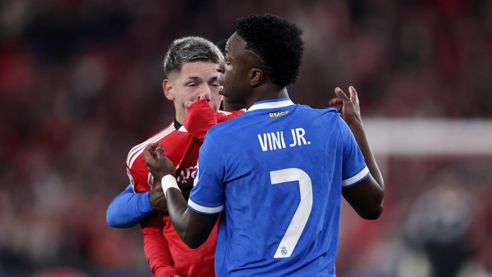 Two soccer players clash on the field: a blue-jersey player with 'VINI JR.' and number 7 facing a red-jersey opponent.