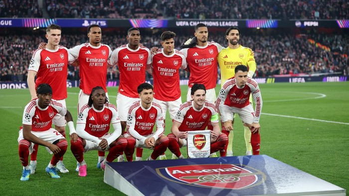 Arsenal players in red and white kits pose for a pre-match team photo on the pitch, with the trophy display in front.
