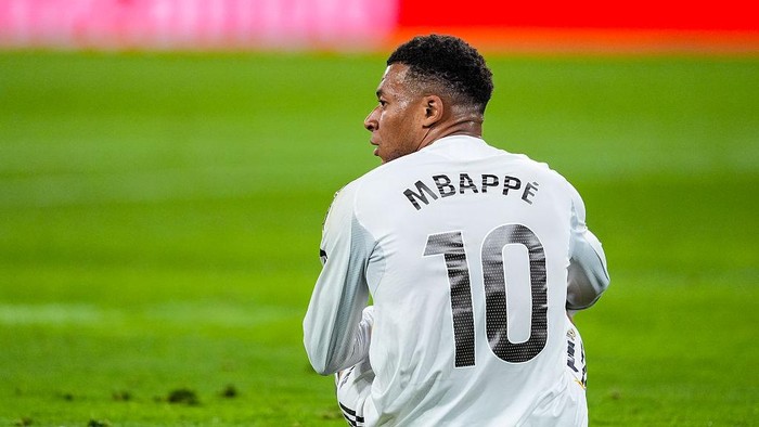 Back view of Kylian Mbappé wearing a white jersey with the number 10 on a green soccer field.