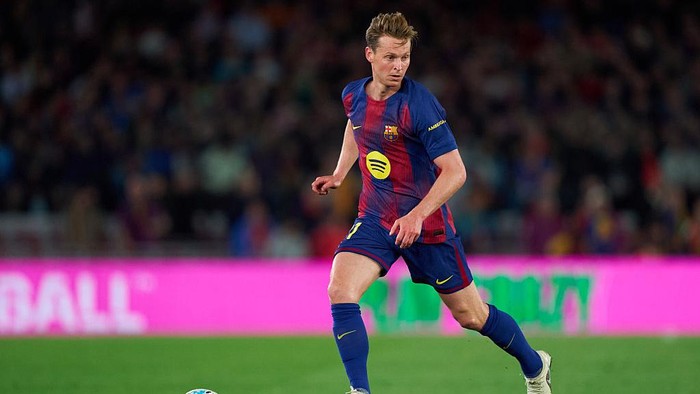 Soccer player in a Barcelona jersey dribbling the ball on a green pitch during a match with a blurred stadium crowd in the background.