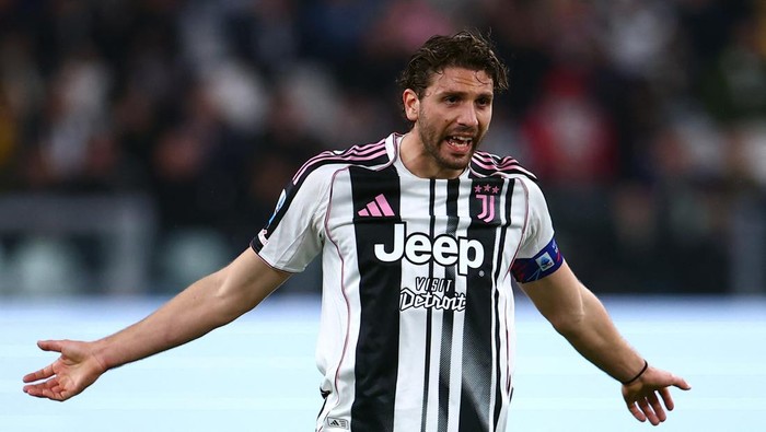 Juventus soccer player celebrating with arms outstretched on the field in a black-and-white striped kit with captain's armband.