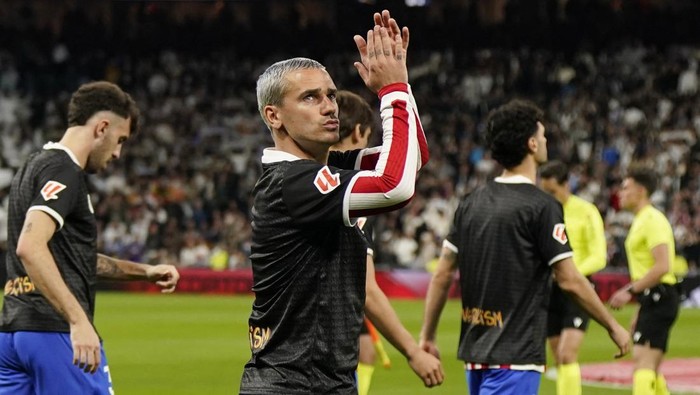 Football players in black uniforms on a pitch applaud a crowd after a match.