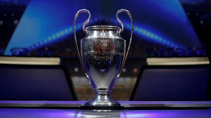 The UEFA Champions League trophy on a pedestal under blue stage lights.