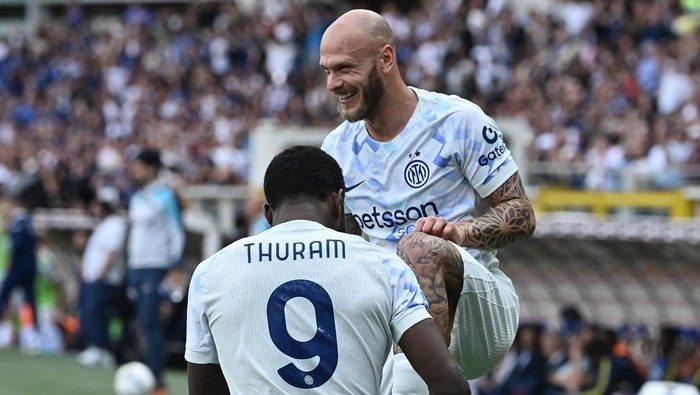 Two soccer players in light blue Inter Milan jerseys celebrate on the field as the crowd cheers in the background.
