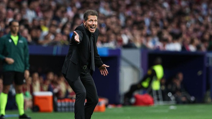 Soccer manager in a suit shouting and pointing from the touchline during a match.