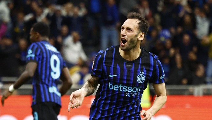 Inter Milan player in blue-and-black stripes celebrates on the pitch after a goal, shouting with arm outstretched (teammate visible in the background).
