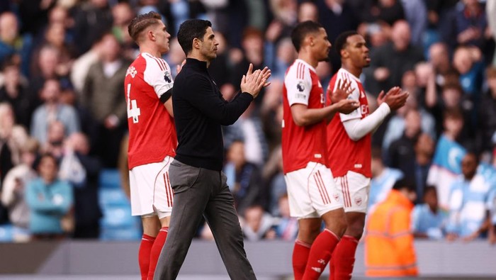 Soccer team clapping on the field after a game, players in red and white kits with a coach in dark clothing at the center.