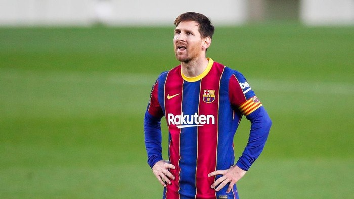 Soccer player in a Barcelona jersey with blue and red stripes standing on a green field, hands on hips, captain's armband visible on the left arm.