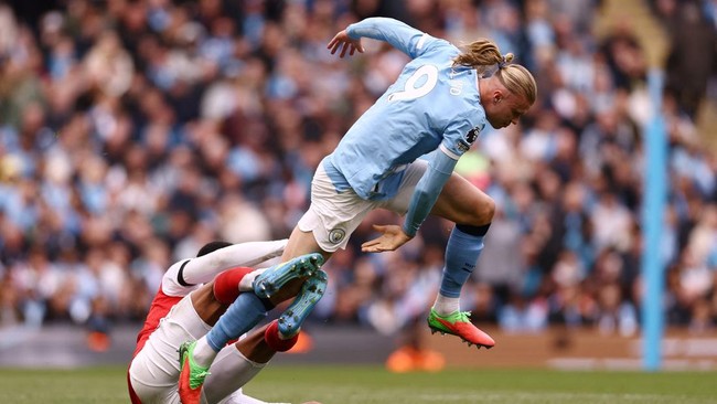 Soccer player in a light blue jersey leaps in the air over a defender during a match.