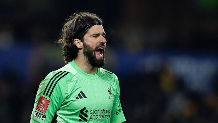 Liverpool goalkeeper Alisson Becker shouts on the field in a bright green kit during a match.