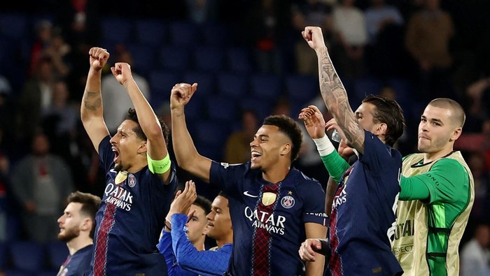 Paris Saint-Germain players celebrate a goal, fists raised in the air on the pitch, blue kits with Qatar Airways logos.