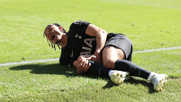Soccer player in a black kit lying on the grass, grimacing in pain after an injury.