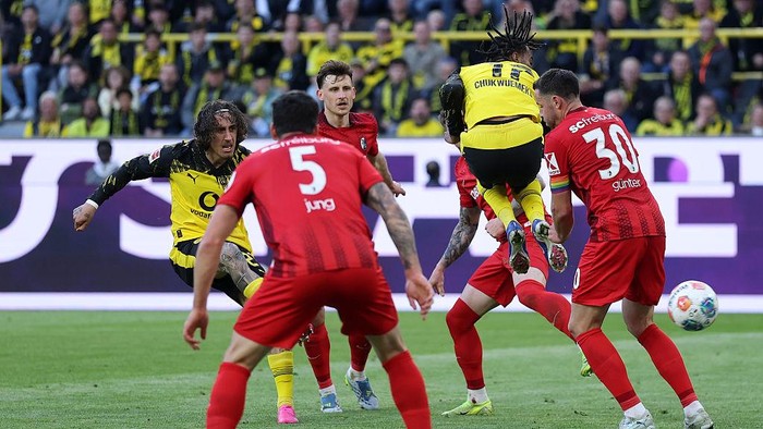 Borussia Dortmund player in yellow and black leaps to challenge the ball amid red-clad opponents during a crowded field moment.