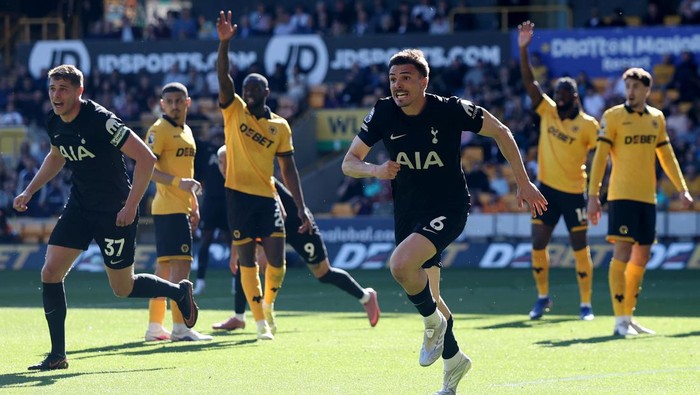 Soccer players in black kits run across a sunny field while opponents in yellow look on, during a match celebration.
