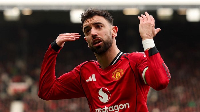 Manchester United footballer in a red home kit celebrates with hands near his head on the pitch after a goal.