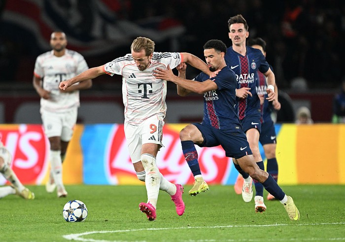 Soccer players from Bayern Munich (white kit) and Paris Saint-Germain (blue kit) chase the ball during a match on a grassy field in action.
