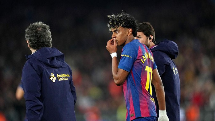Soccer player in FC Barcelona colors (number 11) walks off the pitch with medical staff nearby during a match.