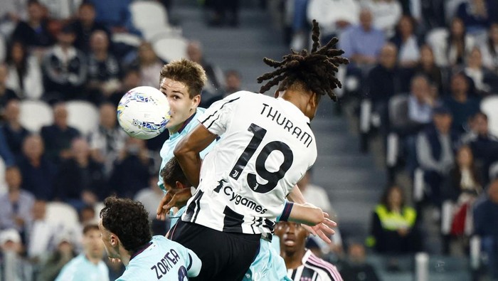 Soccer players leap for a header during a match, with a player wearing number 19 on a white and black striped jersey in the foreground.