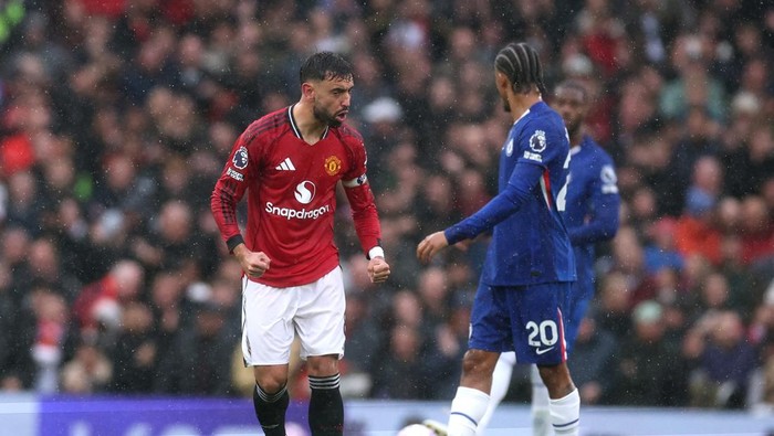 Manchester United player in red challenges a blue-jersey opponent for the ball during a match in a stadium.