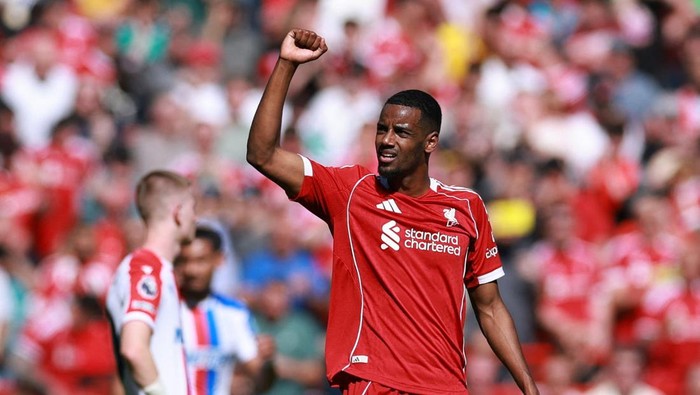 Liverpool footballer in a red kit raises his fist in celebration on the pitch.