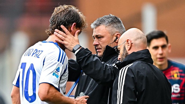 Soccer coach with headset checks on a player wearing jersey number 10 after an injury during a match.