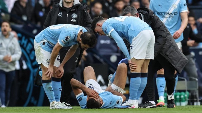 Manchester City players surround an injured teammate lying on the grass during a match.
