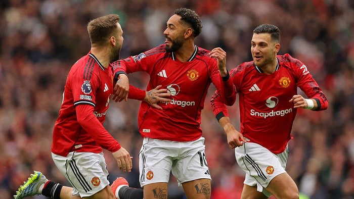 Manchester United teammates celebrate a goal on the pitch, red jerseys and crowd in the background