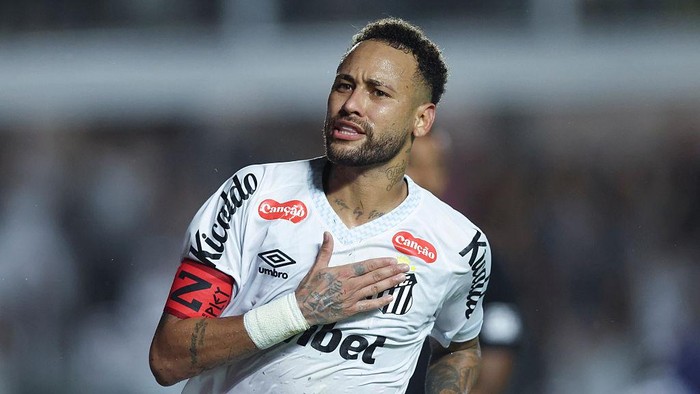 Soccer player in a white Santos jersey with captain armband, hand over heart during a match.