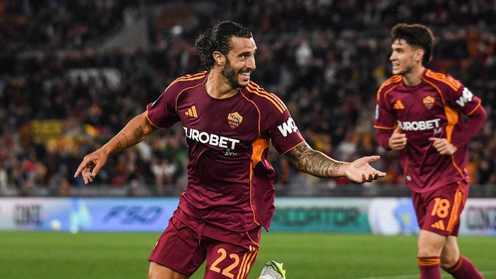Two AS Roma players in maroon kits celebrate on the soccer field during a match.