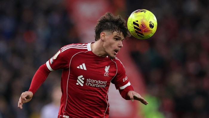 Liverpool FC player in a red kit heading a bright yellow ball during a match, stadium in background.
