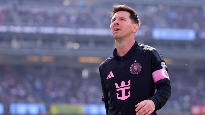 Soccer goalkeeper in a black kit with a pink crest and pink captain's armband, looking upward on the field.
