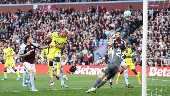 Soccer match scene with players in yellow and maroon challenging near the goal as the ball flies toward the net and the goalkeeper dives.