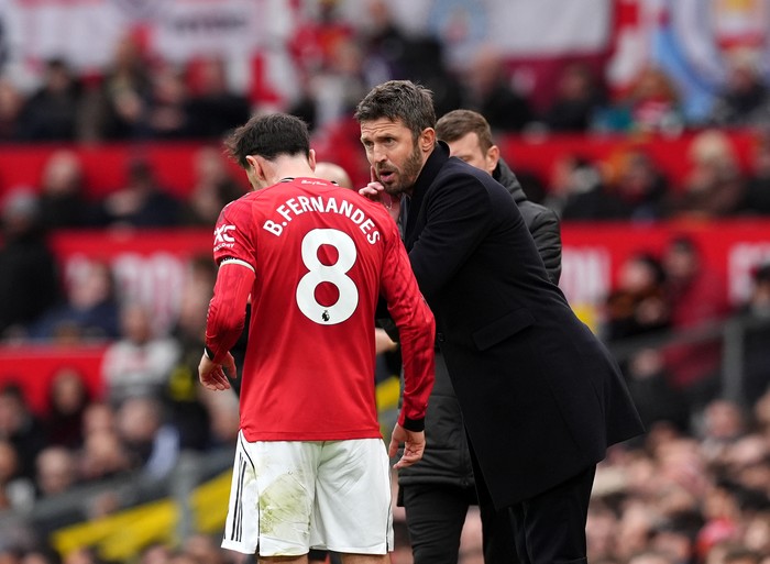 Coach in a black coat talks to a red-kit player wearing number 8 on the field during a match.