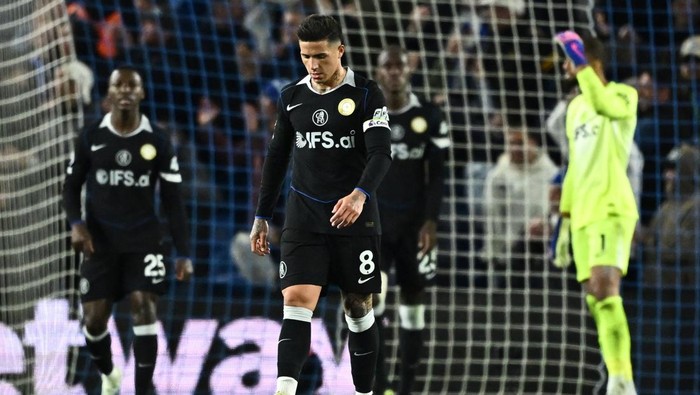 Soccer player in a black PSG jersey with number 8 walking on the field, teammates and a goalkeeper in neon green in the background.