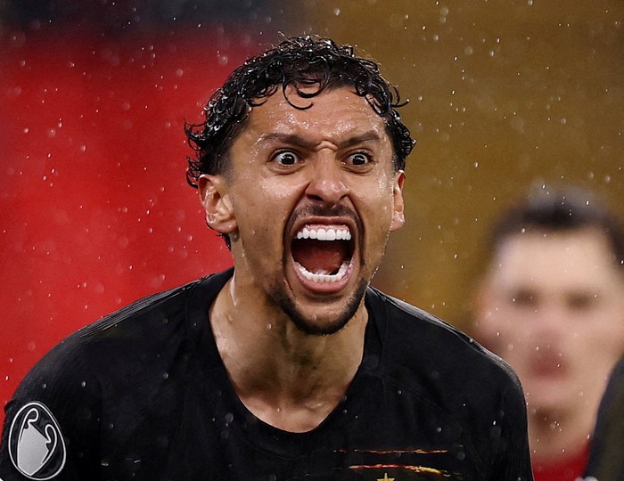 Athlete in a black jersey shouting with mouth wide open in a rain-soaked moment on the field.