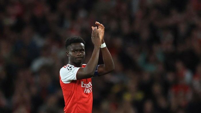 Arsenal footballer in red jersey applauding on the field during a match with a blurred crowd in the background