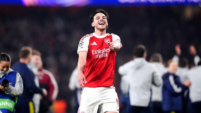 Arsenal footballer in a red jersey celebrates with arms outstretched on the pitch, Emirates Fly Better visible on the shirt.