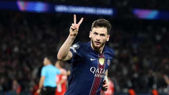 Soccer player in a PSG jersey celebrating on the field, making a two-finger peace sign at the crowd.