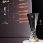 UEFA Europa League trophy on a pedestal with a large bracket diagram behind it labeled 'Road to Istanbul' and team names.